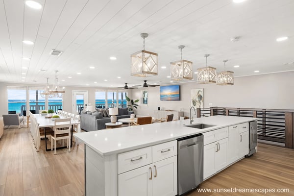 Open-plan kitchen, dining, and living area with ocean view, white cabinetry, island, and coastal decor