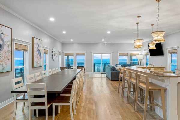 Open-plan dining and kitchen area with ocean views, wooden floors, white cabinetry, and woven pendant lights