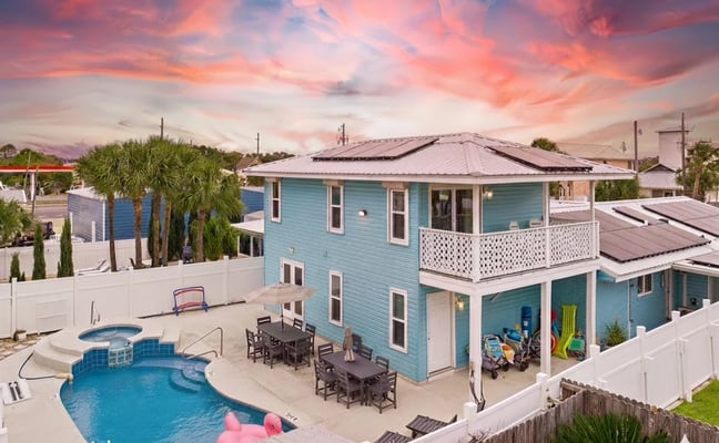 Turquoise two-story beach house with pool, hot tub, and covered patio at sunset